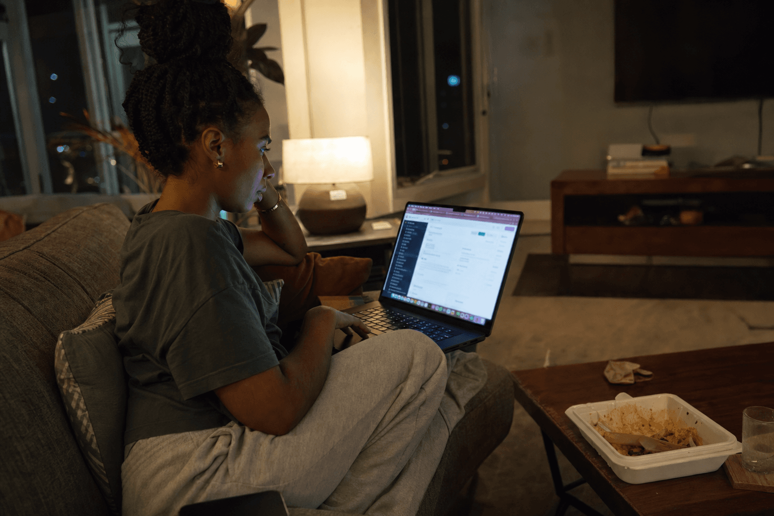 Person on a couch at night with a laptop, takeout on the coffee table, and a phone beside them while working on a product
