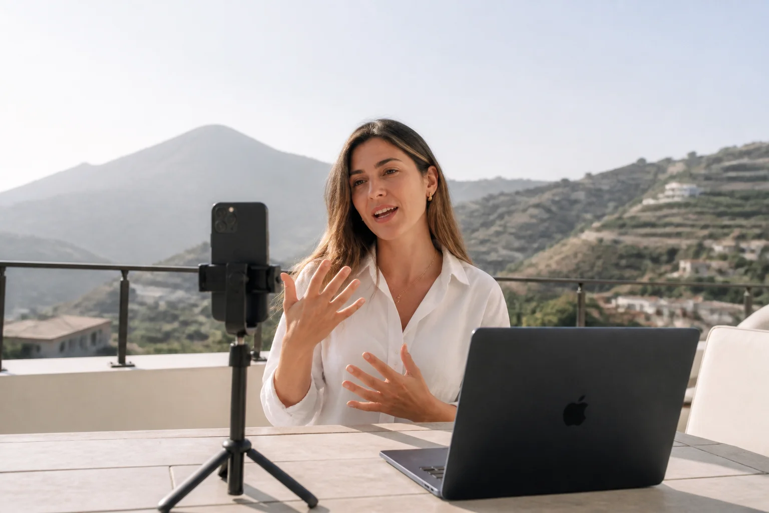 Solo founder on a forest terrace desk filming a phone screen with a ring light, laptop and large monitor showing a vertical video timeline beside sticky notes labeled hook and bio link