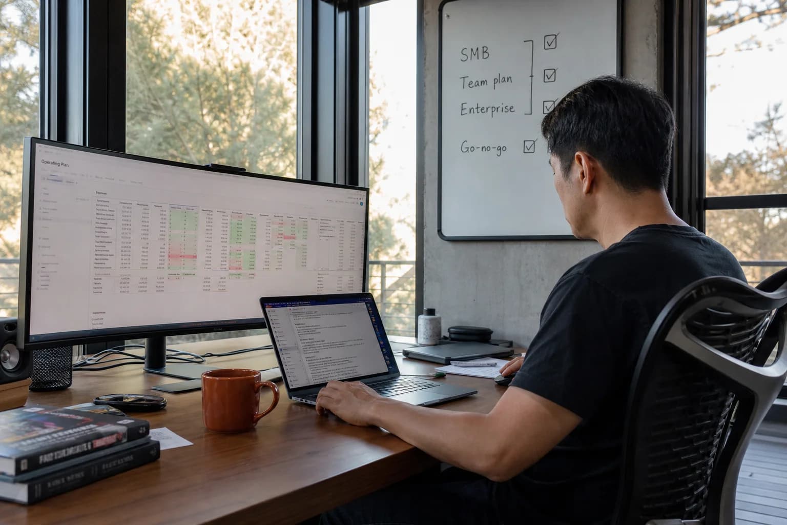 Solo founder at a desk with a whiteboard showing SMB, team plan, and enterprise tiers with go-no-go gates, coffee cup and laptop nearby