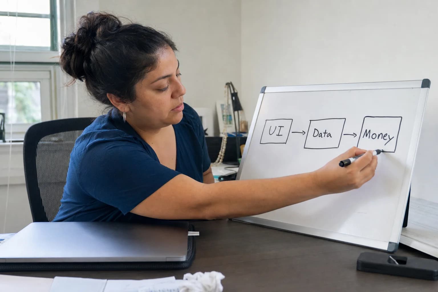 Person sketching three labeled boxes for UI, data, and payments on a whiteboard beside a closed laptop